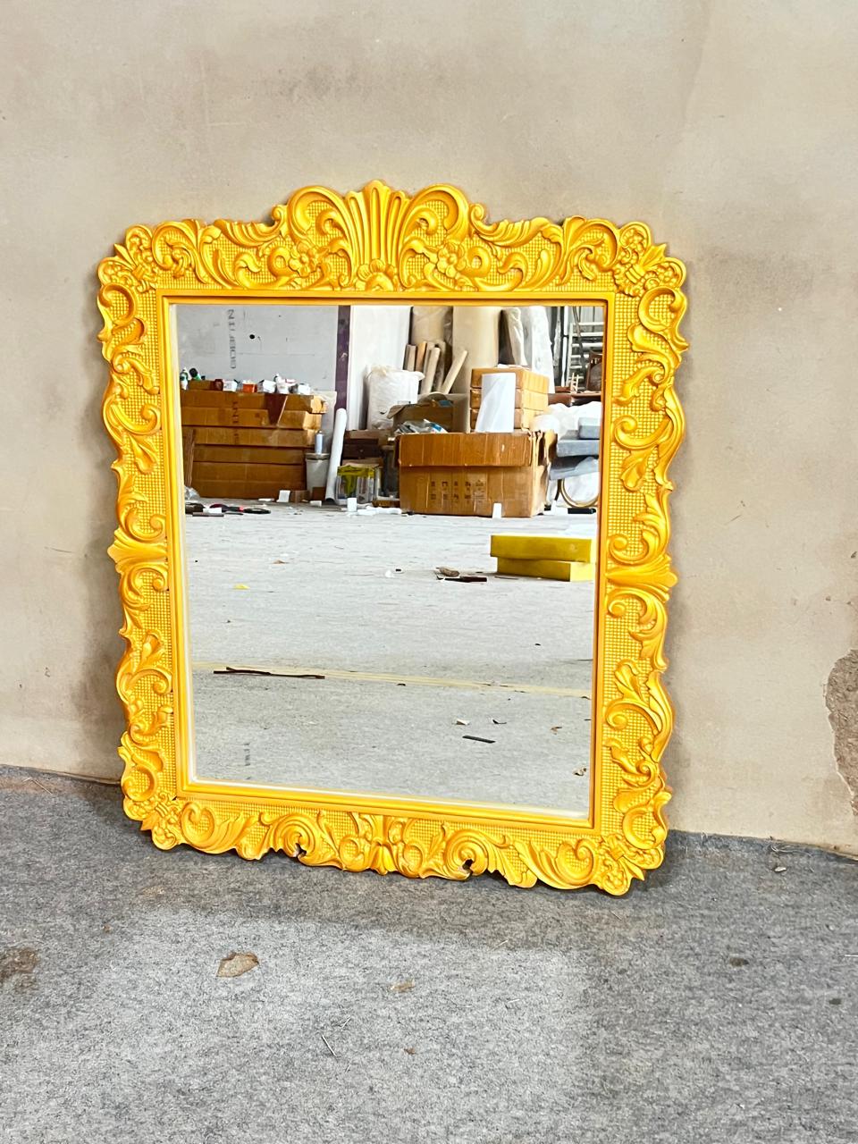 Yellow ornate mirror on a gray floor with a neutral wall background