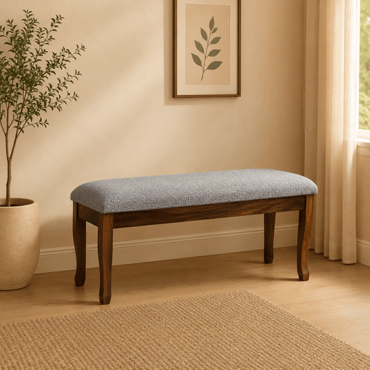 Wooden bench with gray cushion in a room with a plant and framed picture on the wall.