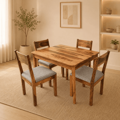 Wooden dining table with four chairs in a room with a plant and framed picture on the wall.