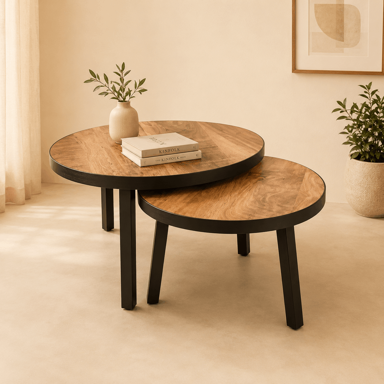 Two wooden coffee tables with a plant and books in a room with beige walls and a framed picture.