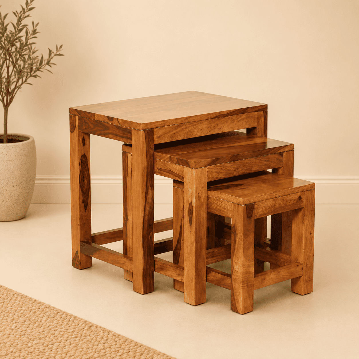 Set of three wooden nesting tables on a beige floor with a plant in the background