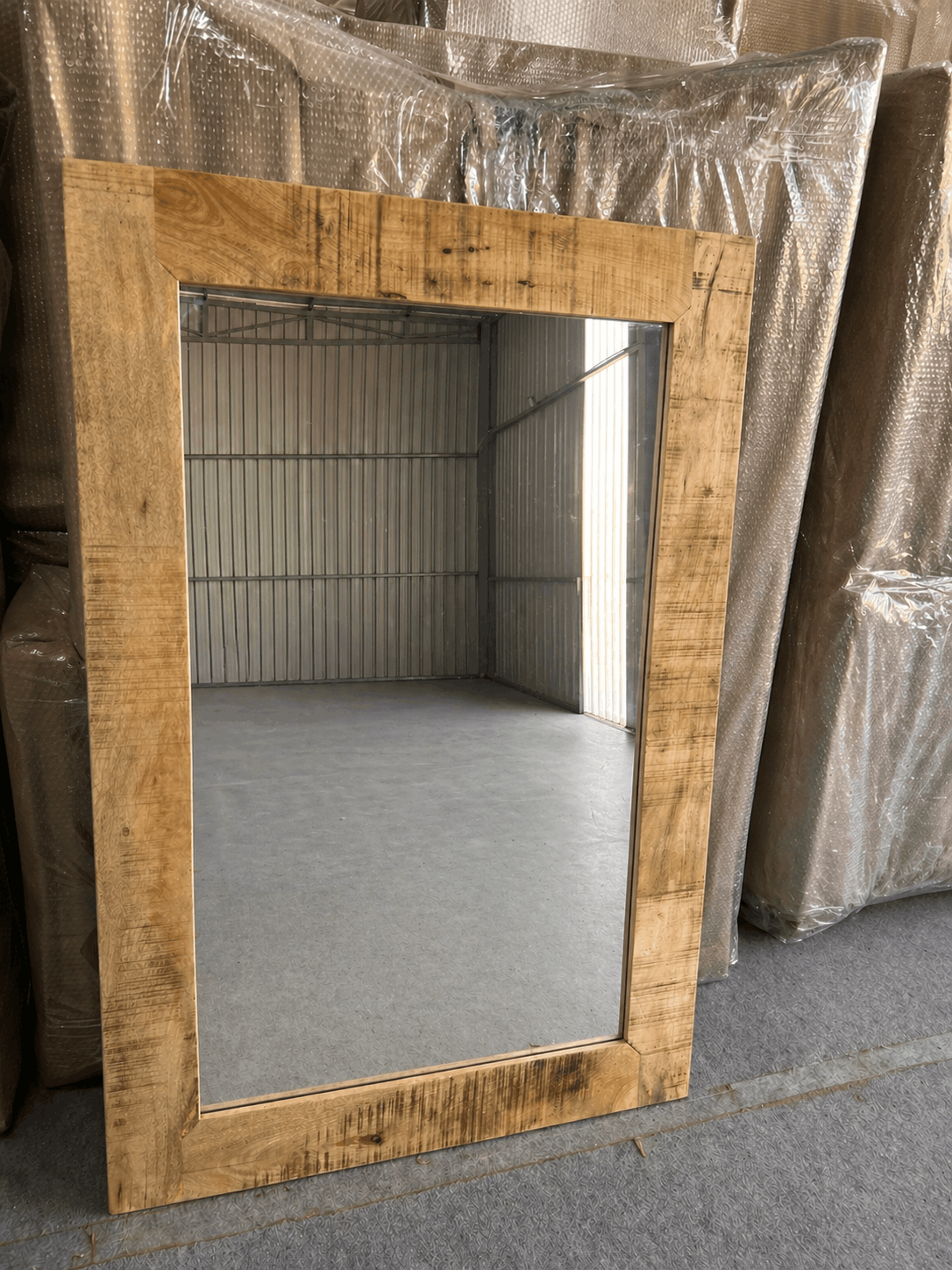 Wooden-framed mirror leaning against a metallic wall.